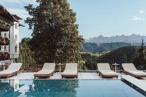 Zona junto a la piscina con sillas de descanso y vistas a montañas.