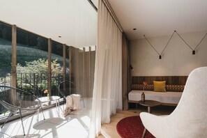 Una sala de estar moderna con un ventanal grande, un sofá, un sillón blanco y un comedor con mesa y sillas.