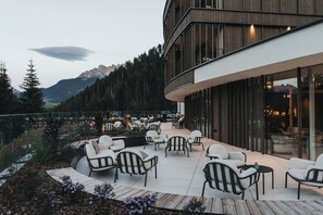 Un área de estar moderna al aire libre con sillas y mesas, con vistas a un paisaje montañoso.