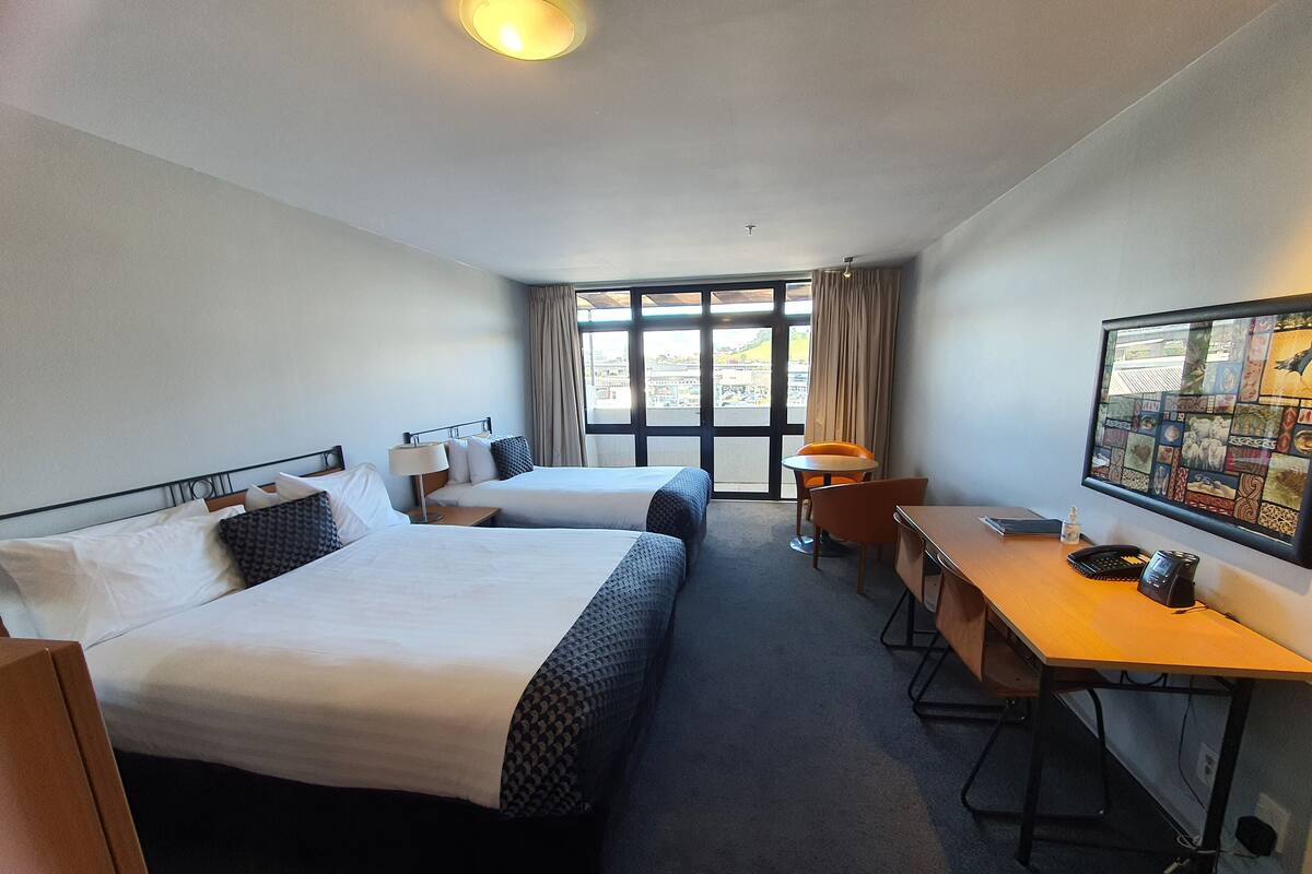 A hotel room with two beds, a desk, a chair, and a large window with curtains.