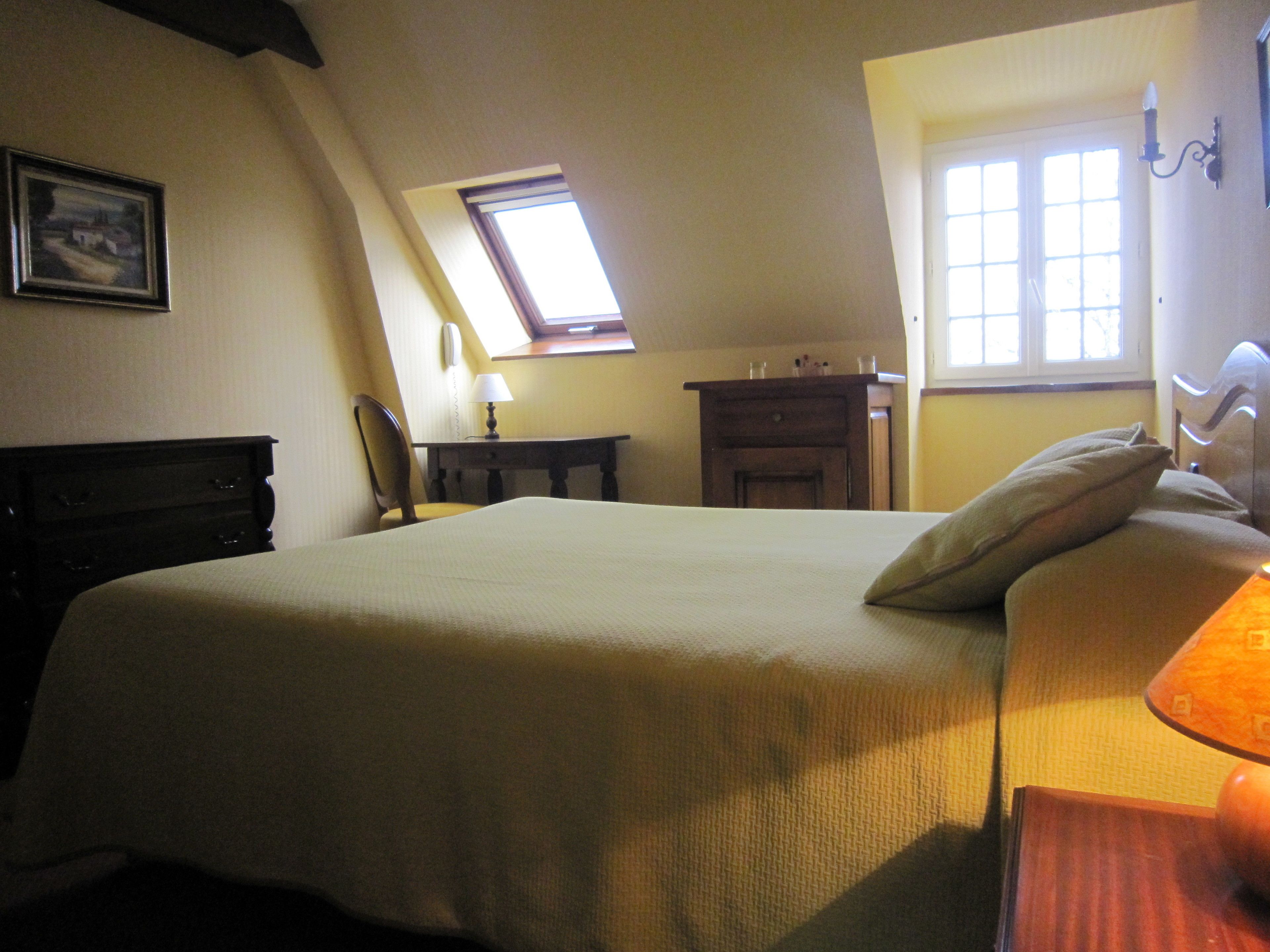 Una camera da letto con un letto grande, una scrivania, una sedia, un comodino, una lampada, una finestra e un quadro appeso al muro.