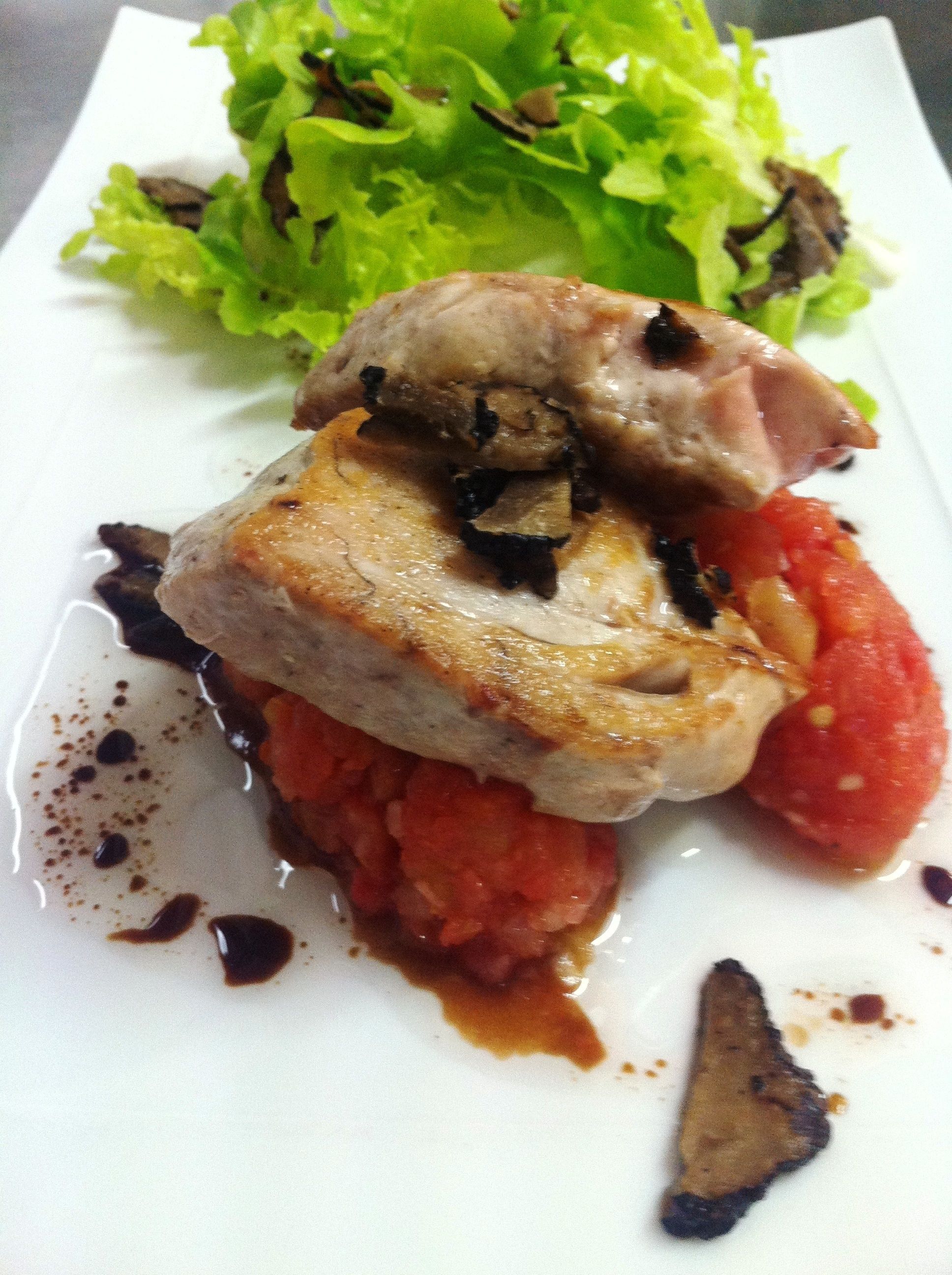 A plate with a piece of meat, a slice of tomato, and some greens.