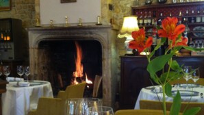 A dining area with a fireplace, a table set for a meal, and a vase with flowers. - Hostellerie de la Bouriane (Gourdon)
