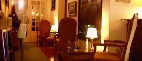 A hotel lobby with a wooden floor, a reception desk, and several armchairs.
