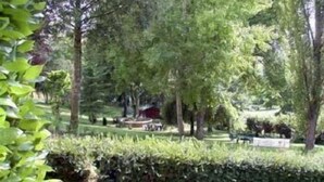 A park with trees, a bench, and a building in the background. - Hostellerie de la Bouriane (Gourdon)