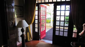 Vista del interior de un vestíbulo de hotel con una puerta de madera que da al exterior, una lámpara y un cuadro en la pared.