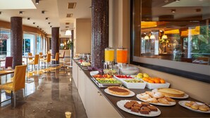 Un bufet amb una varietat d'aliments i begudes, una zona de seients amb cadires i un gran finestral que ofereix una vista de l'exterior.
