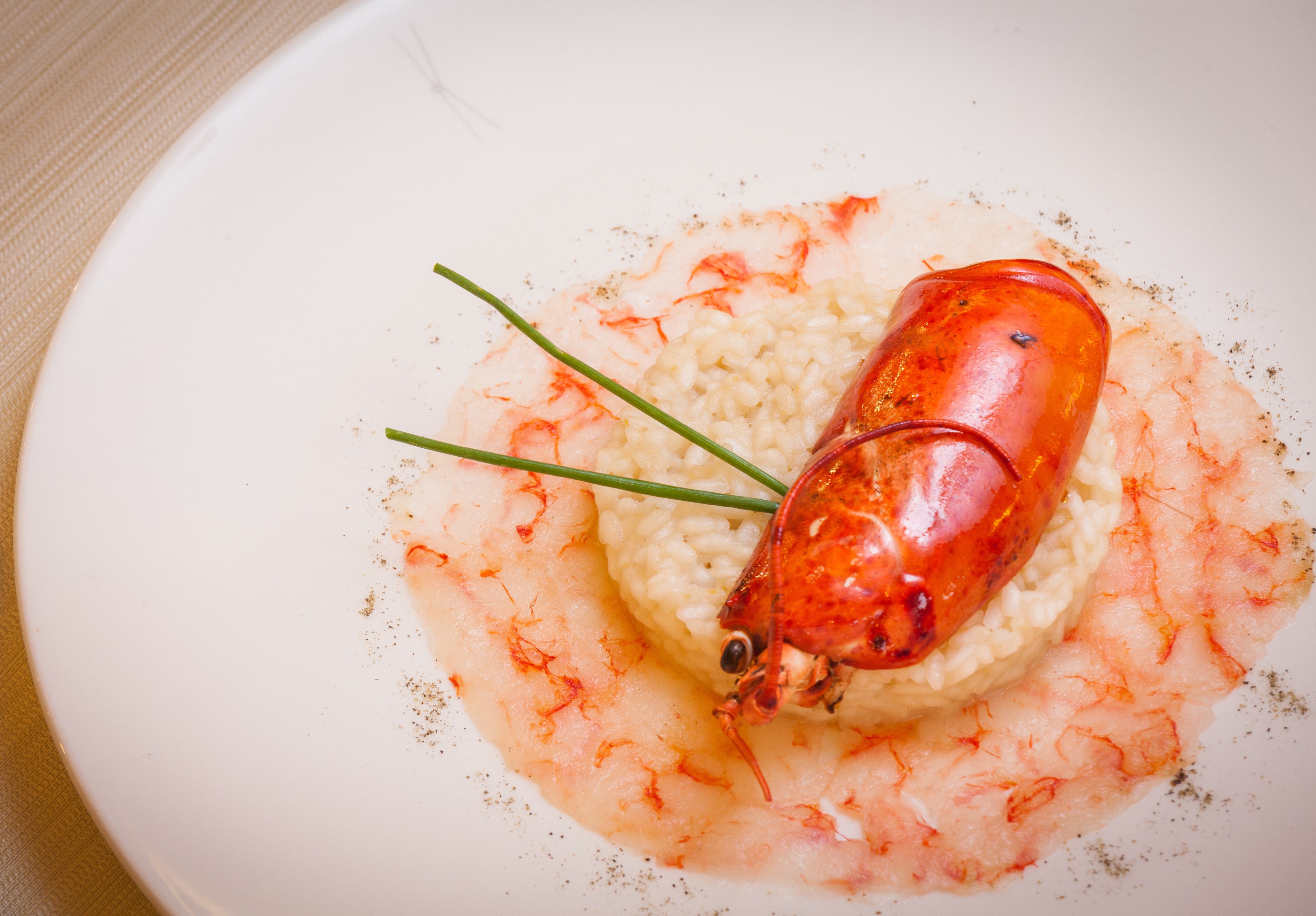 A plate with a lobster tail on top of a bed of rice, garnished with green herbs and sprinkled with seasoning.