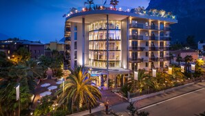 Hotel de diverses plantes amb façana corba, balcons i un pati ajardinat amb palmeres.