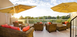 Ein Balkon mit Korbmöbeln und gelben Sonnenschirmen mit Blick auf eine Stadtlandschaft.