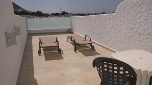 A rooftop terrace with two sun loungers and a table, surrounded by a white textured wall and a view of a distant landscape. - Hostal Las Gaviotas (Nijar)