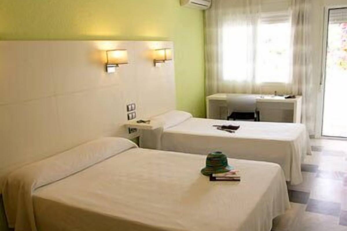 Habitación de hotel con dos camas, un escritorio y una ventana con cortinas.