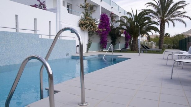 A swimming pool with a metal ladder, surrounded by a tiled patio with outdoor seating and palm trees. - Hostal Las Gaviotas (Nijar)