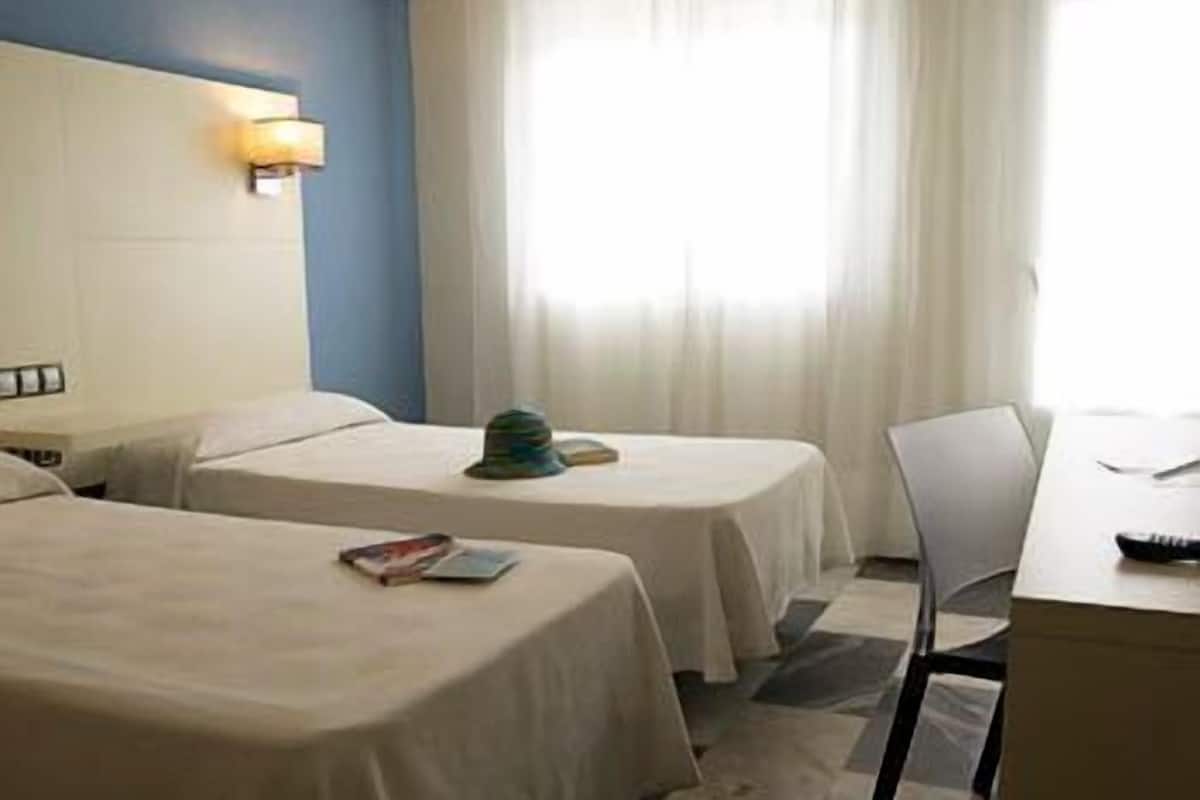 Habitación de hotel con dos camas individuales, un escritorio y una silla.