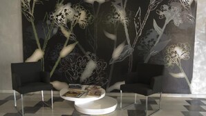 A modern lobby with two black chairs, a white round table, and a large floral mural on the wall. - Hostal Las Gaviotas (Nijar)