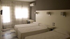 A hotel room with three beds, a desk, and a window with curtains. - Hostal Las Gaviotas (Nijar)