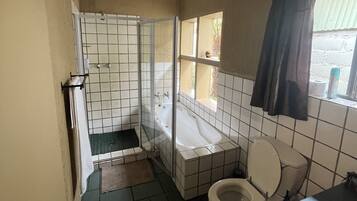 A small, tiled bathroom with a toilet, a shower enclosure, and a window.