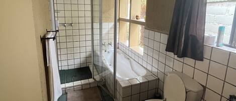 A small, tiled bathroom with a toilet, a shower enclosure, and a window.