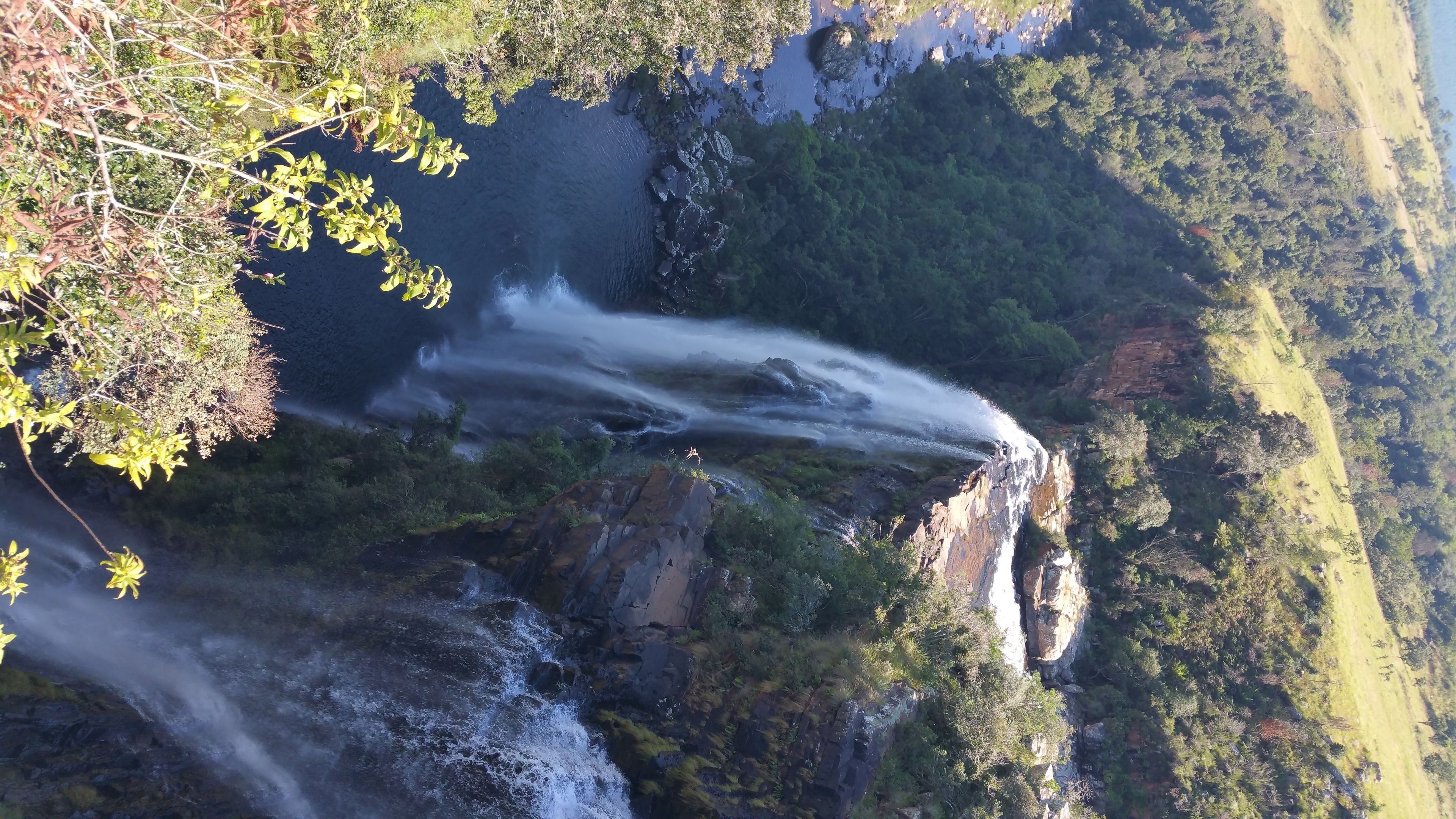 Una cascada que se precipita por un risco rocoso rodeado de abundante vegetación.