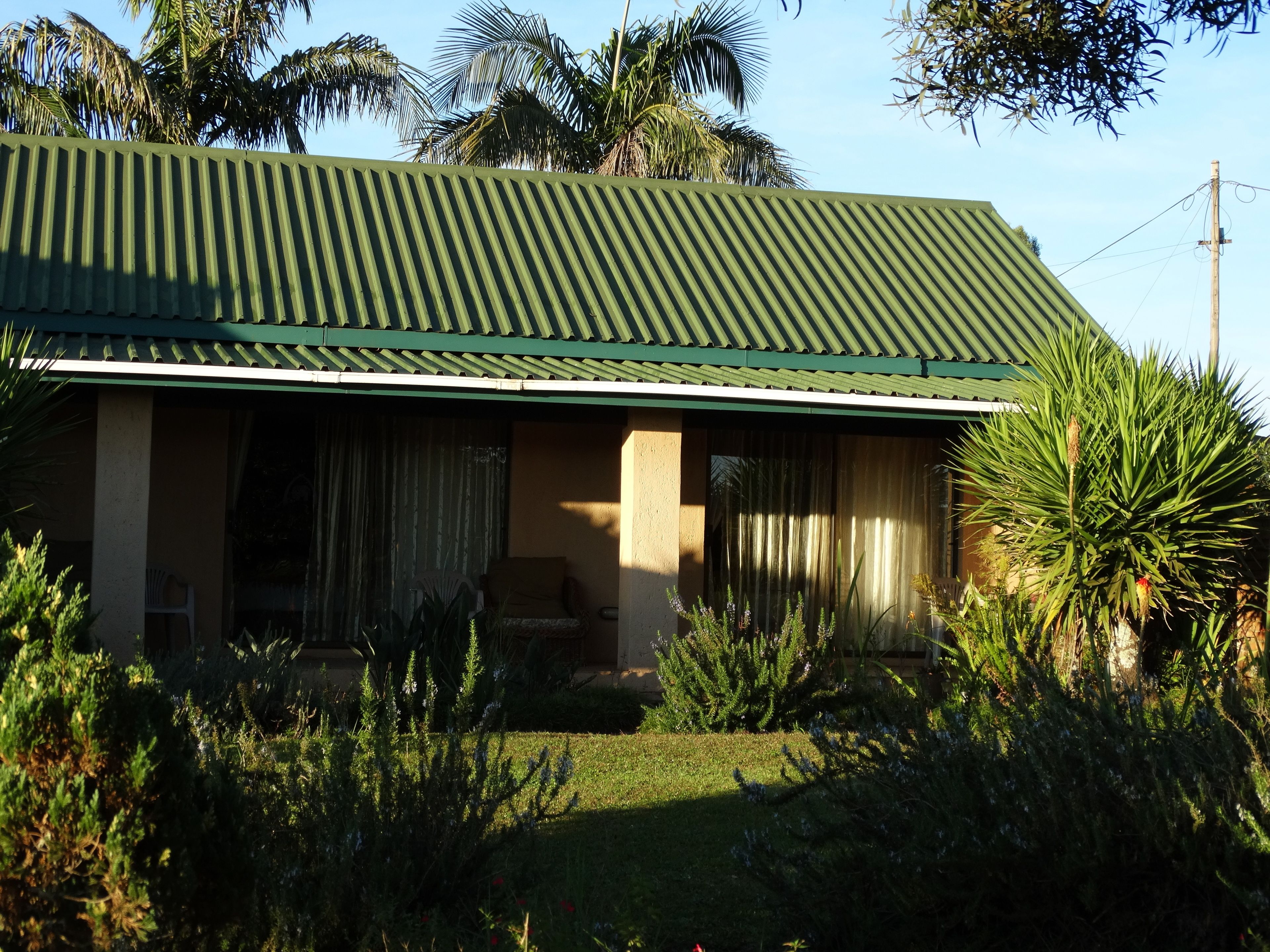 A house with a green roof, a covered porch, and a garden with various plants.