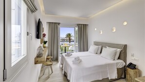 Habitación de hotel moderna con dos camas, un escritorio con silla, una mesita pequeña, un balcón con vistas y un televisor montado en la pared.