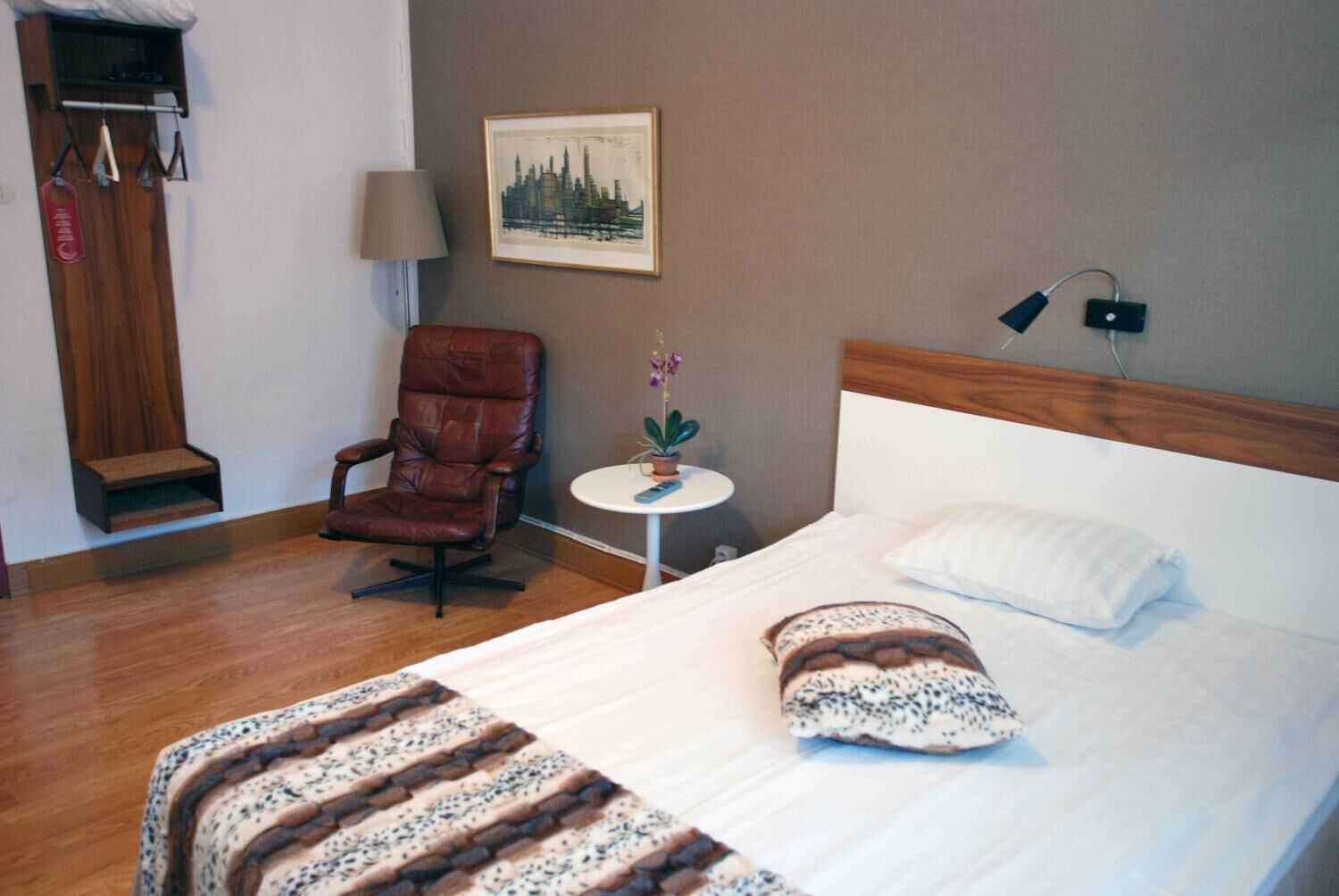 Une chambre d’hôtel avec un lit, une chaise, une petite table avec une plante, une lampe et un tableau au mur.