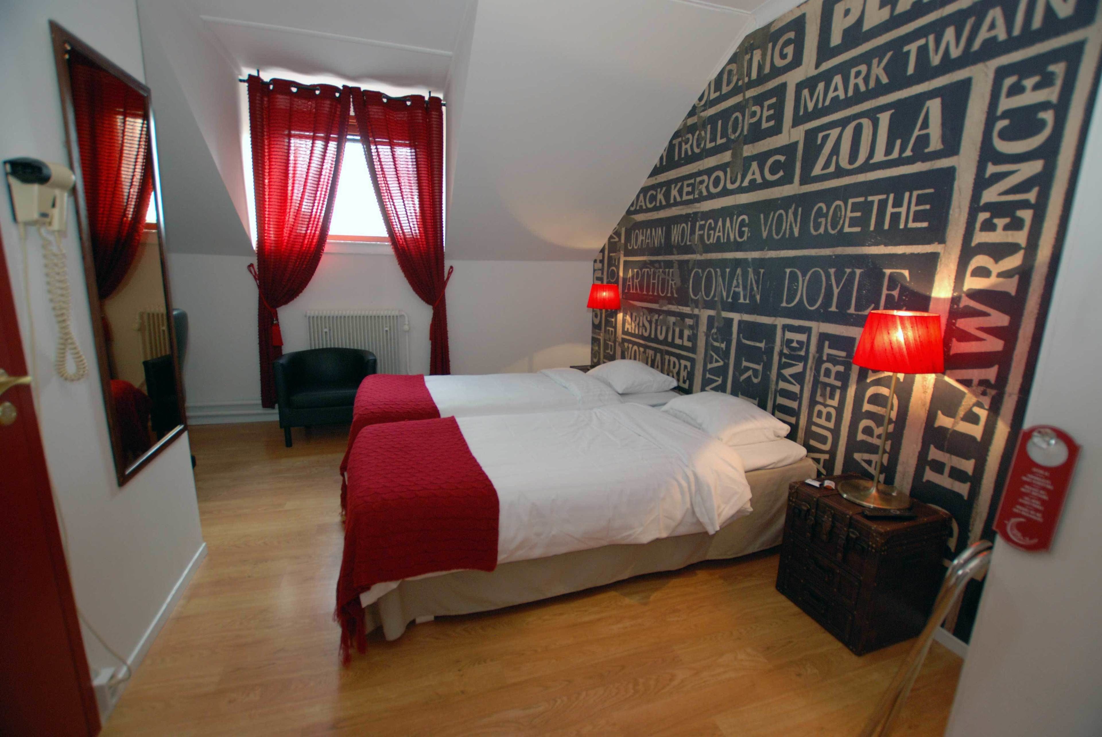 A hotel room with two beds, a red curtain, a mirror, a radiator, and a wall with names.