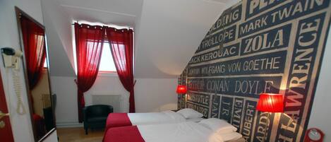 A hotel room with two beds, a red curtain, a mirror, a radiator, and a wall with names.