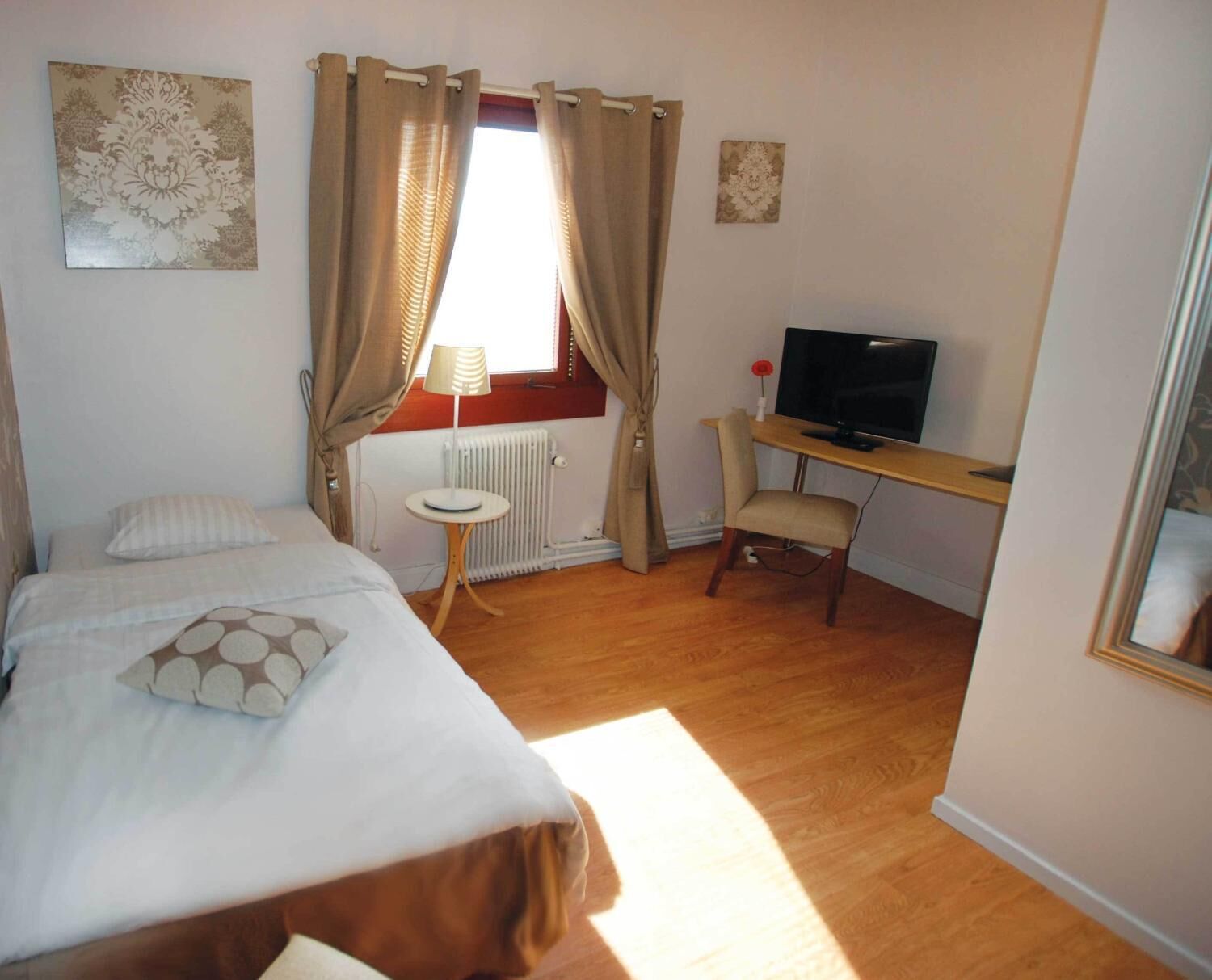 A bedroom with a bed, a desk with a TV, a radiator, and curtains.