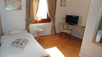 A bedroom with a bed, a desk with a TV, a radiator, and curtains.