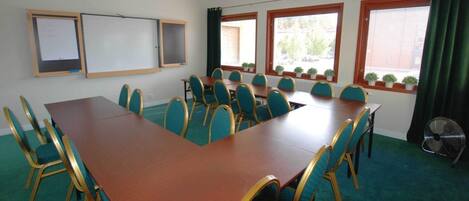 Une salle de conférence équipée d’une longue table, de chaises, d’un tableau blanc et de fenêtres avec des stores.