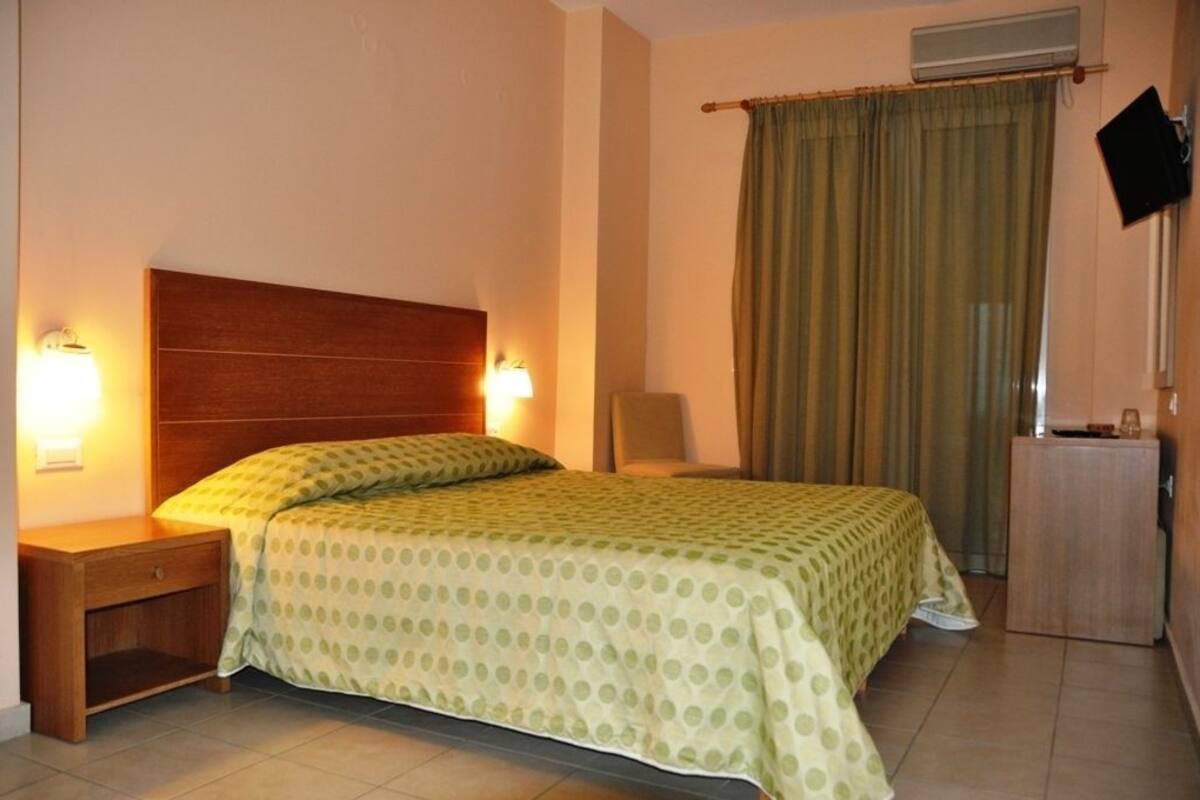 A hotel room with a bed, a nightstand, a desk, a chair, a TV, and a window with curtains.