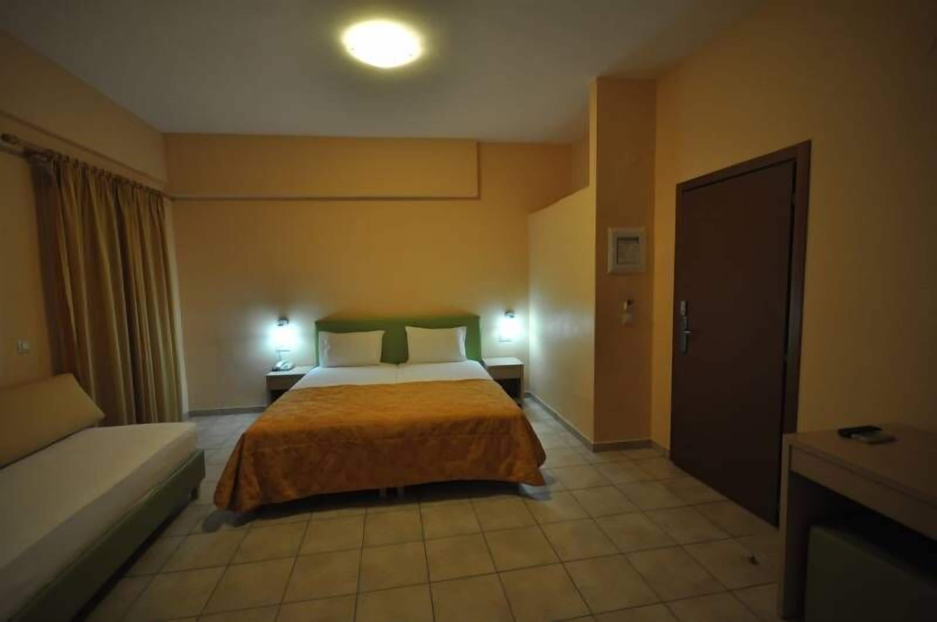 Et hotelværelse med en seng, to sengeborde, et skrivebord, et klædeskab og et gardin.
