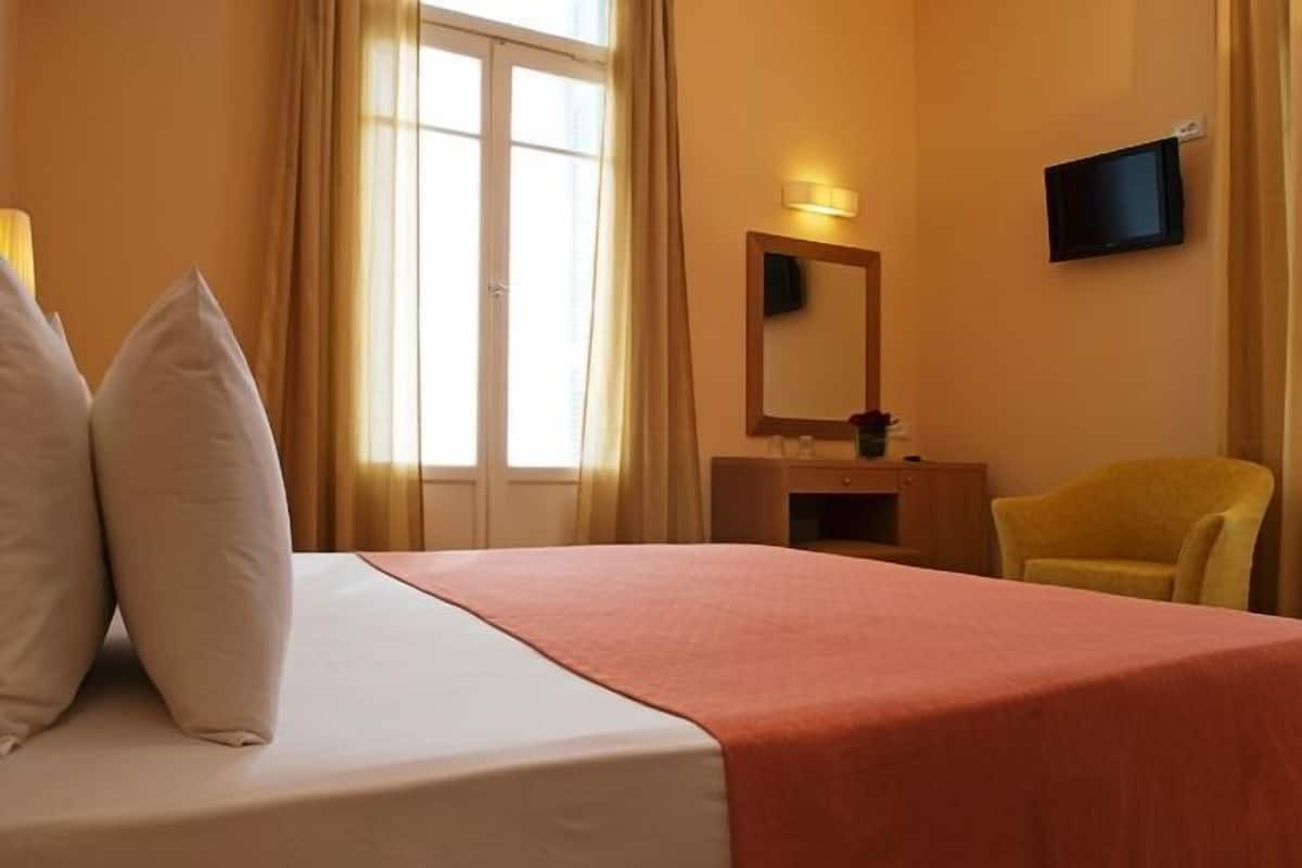 A hotel room with a bed, a television mounted on the wall, a desk with a mirror, and a chair.