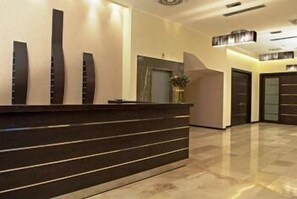 A modern reception area with a dark reception desk, a large vase with flowers, and a clean, polished floor. - Park Hotel (Nafplio)