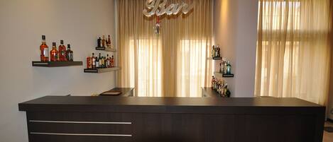 Zona de bar con mostrador de recepción, estanterías con botellas y un cartel que dice 'Bar'.