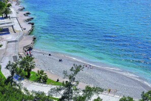 A beach with a paved walkway, palm trees, and a rocky shoreline. - Park Hotel (Nafplio)