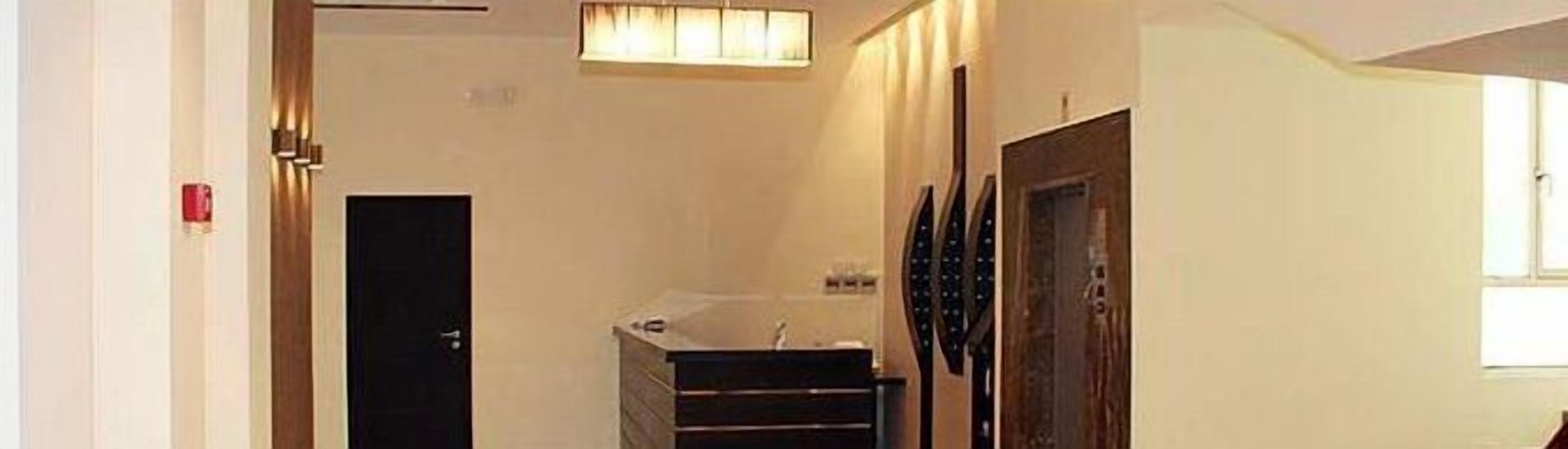 Un pasillo estrecho con una puerta a la izquierda, una escalera con barandilla a la derecha y una lámpara fijada a la pared en la parte superior.