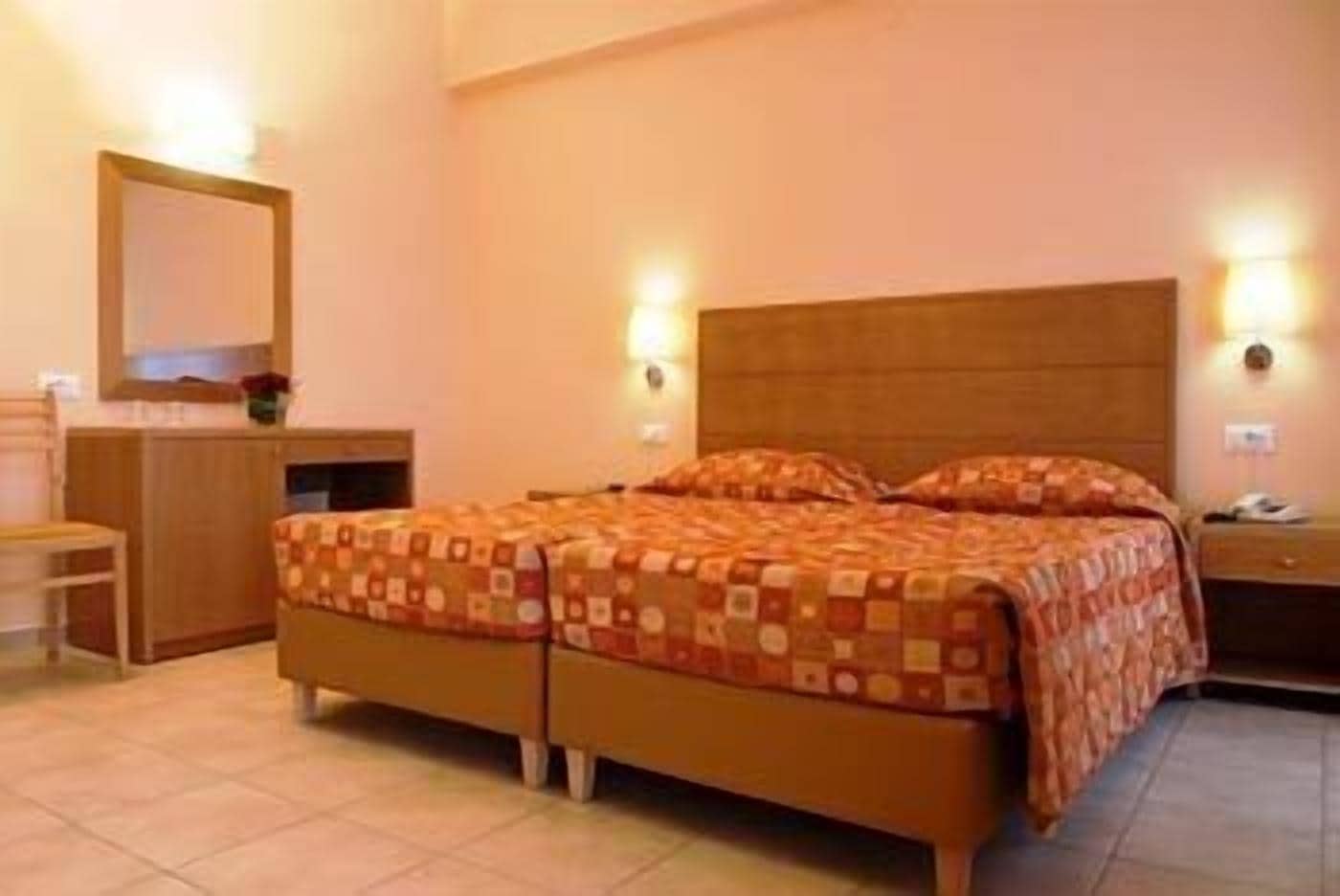 Habitación de hotel con cama doble, mesita de noche, espejo y escritorio.