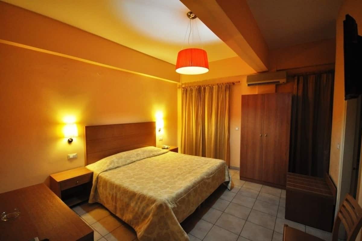 A hotel room with a bed, bedside lamps, a wardrobe, and a hanging light fixture.