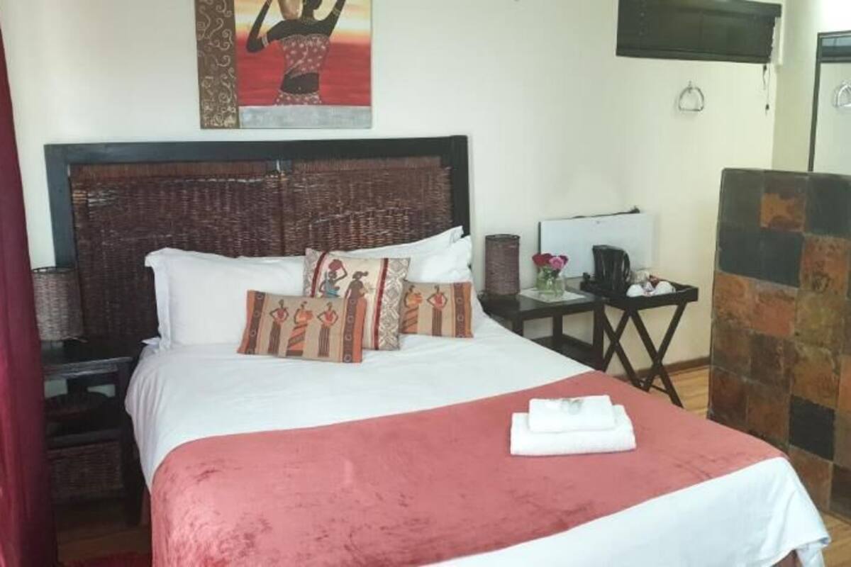 A neatly made bed with a red bedspread and decorative pillows, a nightstand with a lamp, and a small table with a vase of flowers.