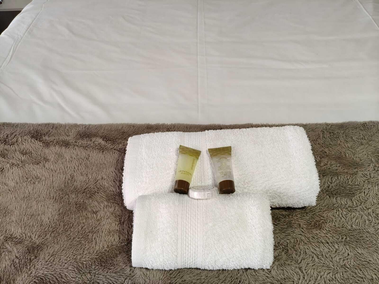 A bed with a white sheet and a brown fluffy blanket. There are two bottles of shampoo and conditioner on the blanket.