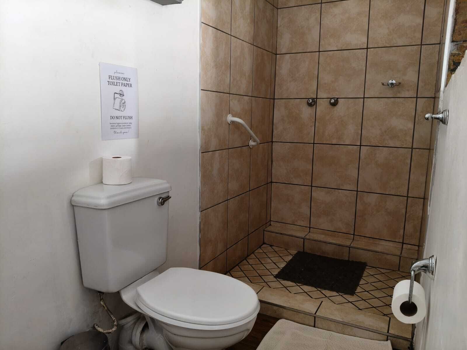 Casa de banho pequena com sanita, cabine de duche e sinal a indicar para deitar apenas papel higiénico.