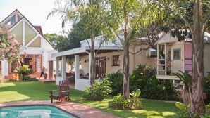 Zona de piscina con un sendero de ladrillo, rodeada de exuberante vegetación y una pequeña terraza de madera.