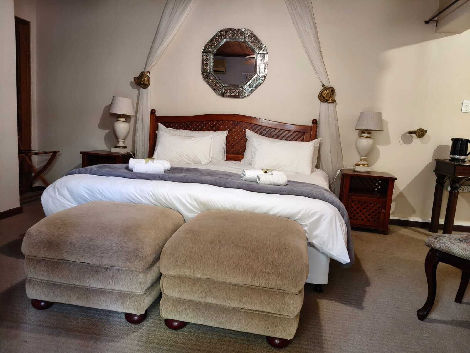 A neatly arranged bedroom with a four-poster bed, two bedside tables, a mirror, and a canopy.