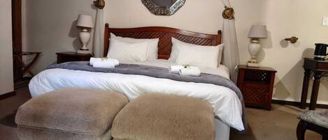 A neatly arranged bedroom with a four-poster bed, two bedside tables, a mirror, and a canopy.
