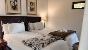 Una cama doble con sábanas blancas, una manta marrón y dos toallas enrolladas. Encima de la cama, en la pared, hay dos cuadros enmarcados con motivos florales.