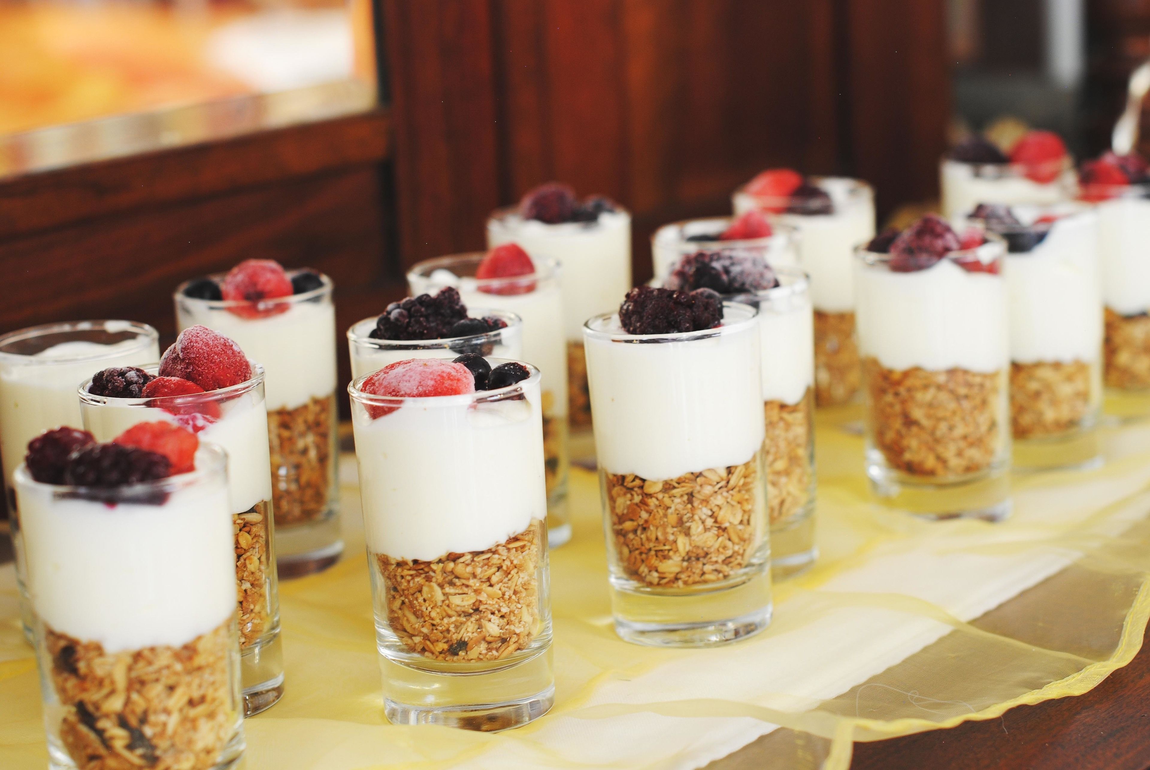 Een rij parfait glazen met granola en bessen op een tafel.