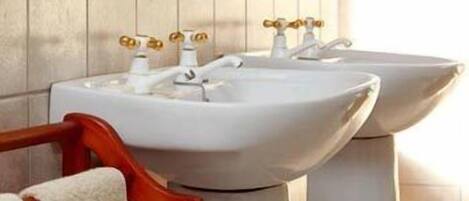 Two white pedestal sinks with gold faucets in a bathroom with wooden paneling.