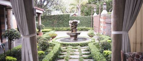 A garden with a fountain, stone pathway, and neatly trimmed hedges.